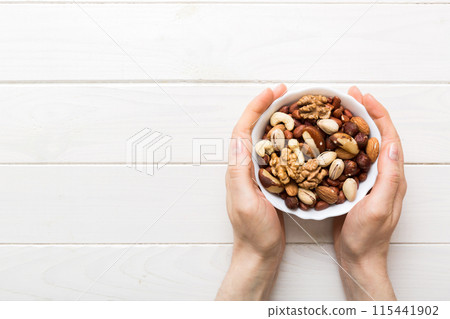 Woman hands holding a wooden bowl with mixed nuts Walnut, pistachios, almonds, hazelnuts and cashews. Healthy food and snack. Vegetarian snacks of different nuts Woman hands holding a wooden bowl with mixed nuts Walnut, pistachios, almonds, hazelnuts and cashews. Healthy food and snack. Vegetarian snacks of different nuts 115441902