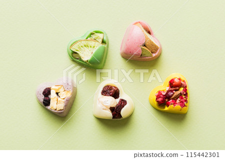chocolate sweets in the form of a heart with fruits and nuts on a colored background. top view with space for text, holiday concept chocolate sweets in the form of a heart with fruits and nuts on a colored background. top view with space for text, holiday concept 115442301