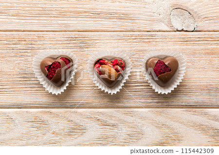 chocolate sweets in the form of a heart with fruits and nuts on a colored background. top view with space for text, holiday concept chocolate sweets in the form of a heart with fruits and nuts on a colored background. top view with space for text, holiday concept 115442309