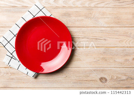 Top view on colored background empty round red plate on tablecloth for food. Empty dish on napkin with space for your design Top view on colored background empty round red plate on tablecloth for food. Empty dish on napkin with space for your design 115442313