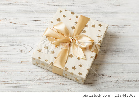 wrapped Christmas or other holiday handmade present in white paper with gold ribbon on colored background. Present box, decoration of gift on colored table, top view with copy space 115442363