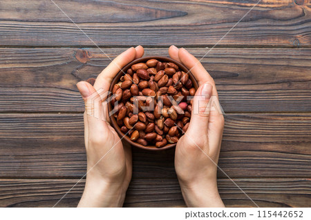 Woman hands holding a wooden bowl with peanuts. Healthy food and snack. Vegetarian snacks of different nuts 115442652