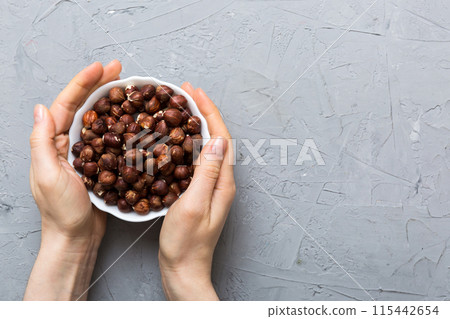Woman hands holding a wooden bowl with hazelnut nuts. Healthy food and snack. Vegetarian snacks of different nuts Woman hands holding a wooden bowl with hazelnut nuts. Healthy food and snack. Vegetarian snacks of different nuts 115442654