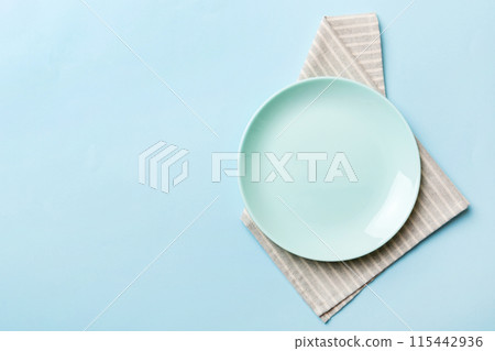Top view on colored background empty round blue plate on tablecloth for food. Empty dish on napkin with space for your design Top view on colored background empty round blue plate on tablecloth for food. Empty dish on napkin with space for your design 115442936