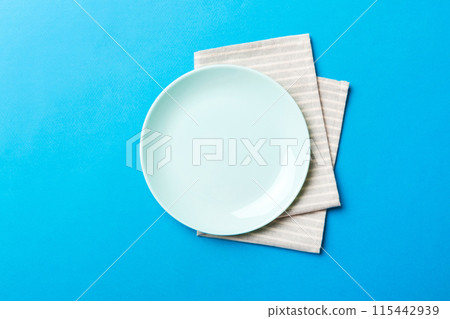 Top view on colored background empty round blue plate on tablecloth for food. Empty dish on napkin with space for your design Top view on colored background empty round blue plate on tablecloth for food. Empty dish on napkin with space for your design 115442939