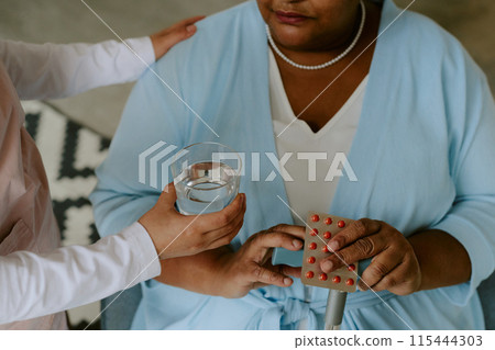 Nurse helping African American female patient with taking pills Nurse helping African American female patient with taking pills 115444303