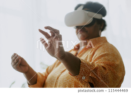 Medium close up photo of senior African American woman imagining her touching things in air using VR headset Medium close up photo of senior African American woman imagining her touching things in air using VR headset 115444469