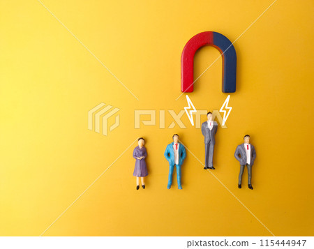 One of miniature people attracts by magnet on a yellow background. Business concept One of miniature people attracts by magnet on a yellow background. Business concept 115444947