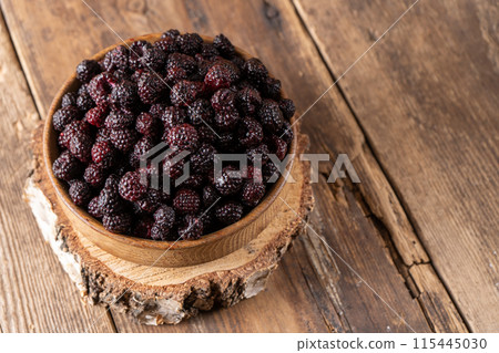 The black berry is a hybrid of raspberries and blackberries. Berries in a wooden bowl on the table. Vitamin summer food. Harvest. Raspberry and blackberry The black berry is a hybrid of raspberries and blackberries. Berries in a wooden bowl on the table. Vitamin summer food. Harvest. Raspberry and blackberry 115445030