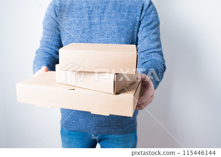 Young anonymous adult delivering three cardboard boxes. White background Young anonymous adult delivering three cardboard boxes. White background 115446144