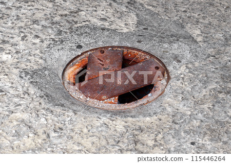 Round drainage well on a concrete road is manually covered with sheets of metal and has a worn rusty appearance Round drainage well on a concrete road is manually covered with sheets of metal and has a worn rusty appearance 115446264