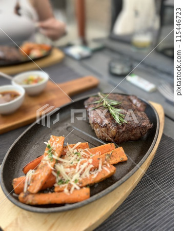 Grilled Steaks with spices rosemary and pepper on wooden board on black background. 115446723