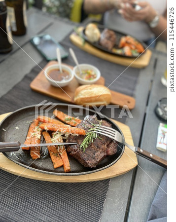 Grilled Steaks with spices rosemary and pepper on wooden board on black background. Grilled Steaks with spices rosemary and pepper on wooden board on black background. 115446726