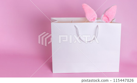 Funny Easter bunny ears in a white paper bag on a pink background. 115447826