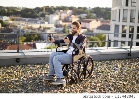 Man in wheelchair taking selfie on rooftop with cityscape background 115448045