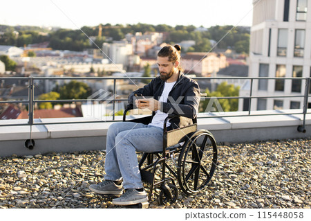 Young man in wheelchair using smartphone on urban rooftop 115448058