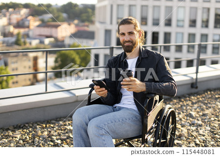 Man in wheelchair using smartphone and holding coffee on rooftop 115448081
