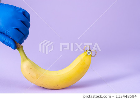 Intimate piercing. Minimal piercing concept. Banana with piercing on purple background Intimate piercing. Minimal piercing concept. Banana with piercing on purple background 115448594