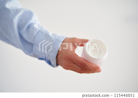Hands in a blue shirt hold a jar of cream. 115448851
