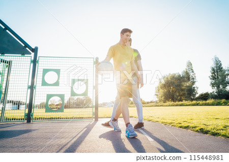 Two Young Caucasian Men Playing Basketball at the Park outdoor playground in sunset light. Teenagers' hobby, offline activity. Concept of sports, hobbies and healthy lifestyle. Selective focus. Two Young Caucasian Men Playing Basketball at the Park outdoor playground in sunset light. Teenagers' hobby, offline activity. Concept of sports, hobbies and healthy lifestyle. Selective focus. 115448981