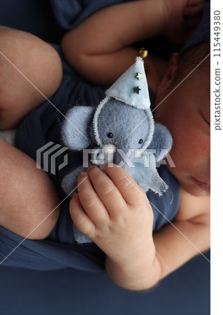 Newborn hands hold a small toy blue elephant. Close-up of a small hand of a child. Rough baby skin. The concept of education, child care and healthcare. Professional macro photo. 115449380