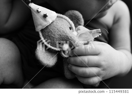 Newborn hands hold a small toy elephant. Close-up of a small hand of a child. Rough baby skin. The concept of education, child care and healthcare. Professional black and white macro photo. Newborn hands hold a small toy elephant. Close-up of a small hand of a child. Rough baby skin. The concept of education, child care and healthcare. Professional black and white macro photo. 115449381