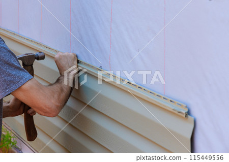 An installation of vinyl PVC siding by handyman during construction new home facade An installation of vinyl PVC siding by handyman during construction new home facade 115449556