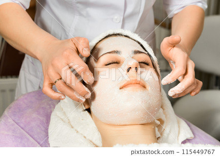 Cosmetologist applying sheet mask on woman's face in beauty salon. Cosmetologist applying sheet mask on woman's face in beauty salon. 115449767