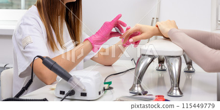 Cosmetologist applying sheet mask on woman's face in beauty salon. 115449779