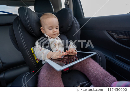 Small girl sitting in the child car seat using a digital tablet device during a long trip Small girl sitting in the child car seat using a digital tablet device during a long trip 115450000