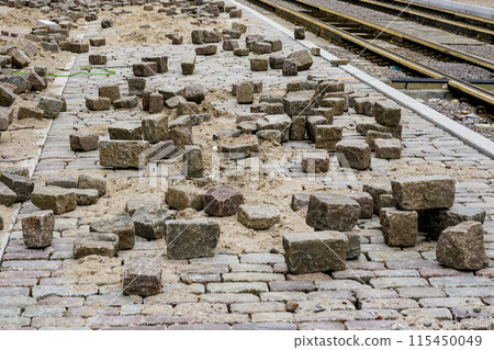 Historic cube shaped hammered natural granite cobblestones on unfinished city street pavement 115450049