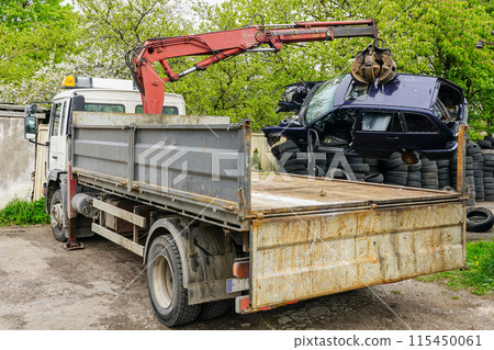 A hydraulic loader loads a abandoned car wreck onto a truck to take it to a recycling site 115450061