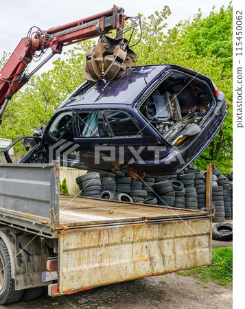 The process of loading an abandoned car wreck using a hydraulic loader mounted on a tow truck 115450062