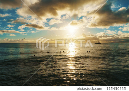 Sun sets, casting warm glow over ocean, boats float in distance 115450335