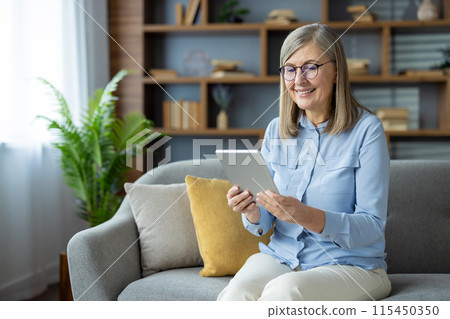 Smiling senior woman using digital tablet at home, sitting comfortably on a sofa. Technology and elderly concept. Smiling senior woman using digital tablet at home, sitting comfortably on a sofa. Technology and elderly concept. 115450350