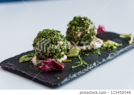 Cheese balls with herbs on a black board on a white background 115450549