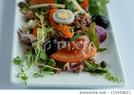 Salad with cabbage, cucumber, egg, onion, tuna and olive oil on a white saucer on a white background 115450621