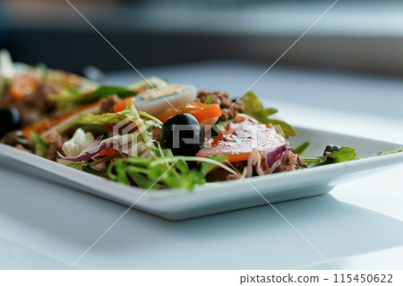 Salad with cabbage, cucumber, egg, onion, tuna and olive oil on a white saucer on a white background 115450622