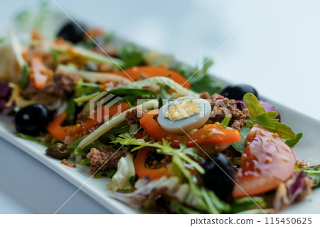 Salad with cabbage, cucumber, egg, onion, tuna and olive oil on a white saucer on a white background 115450625