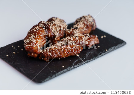 Chicken wings in soy honey sauce with sesame seeds on a black board 115450628