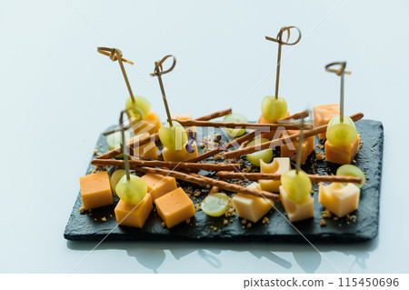 Slicing different types of cheese and grapes. Appetizer with cheese and grapes on a black board 115450696
