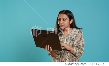 Upbeat woman saluting coworkers, having friendly conversations during teleconference meeting using laptop, studio background. Person discussing during online videocall on notebook device, camera A Upbeat woman saluting coworkers, having friendly conversations during teleconference meeting using laptop, studio background. Person discussing during online videocall on notebook device, camera A 115451140