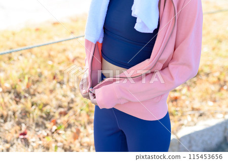 Woman zipping up her hoodie. Young woman walking along the road lined with trees in an autumn park. Cropped. Woman zipping up her hoodie. Young woman walking along the road lined with trees in an autumn park. Cropped. 115453656