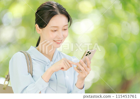 A woman holding a smartphone among the fresh greenery A woman holding a smartphone among the fresh greenery 115453761