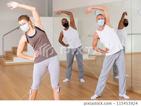 Sporty people in protective masks doing warmups in fitness studio 115453924