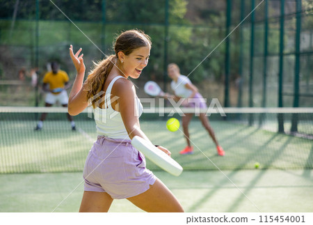 Sportive slim woman with racquet playing padel in court. View from back 115454001