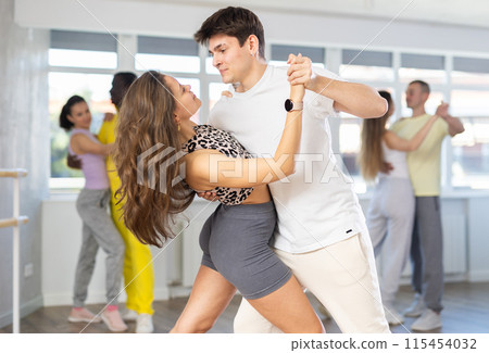 Happy active pair with multinational young men and women dancing and training latin dance movements in ballroom together 115454032