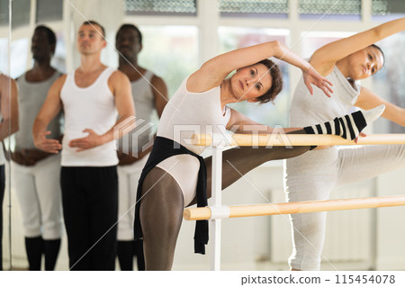 Women performing stretching exercises at ballet barre in studio 115454078