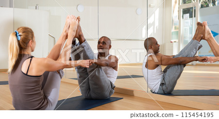 Sporty adult concentrated females and males doing stretching workout in pairs during group training 115454195