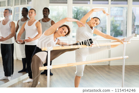 Women performing stretching exercises at ballet barre in studio 115454246